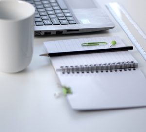 photographie d'un calepin, d'un trombone, d'un crayon à papier, d'une tasse et d'un ordinateur